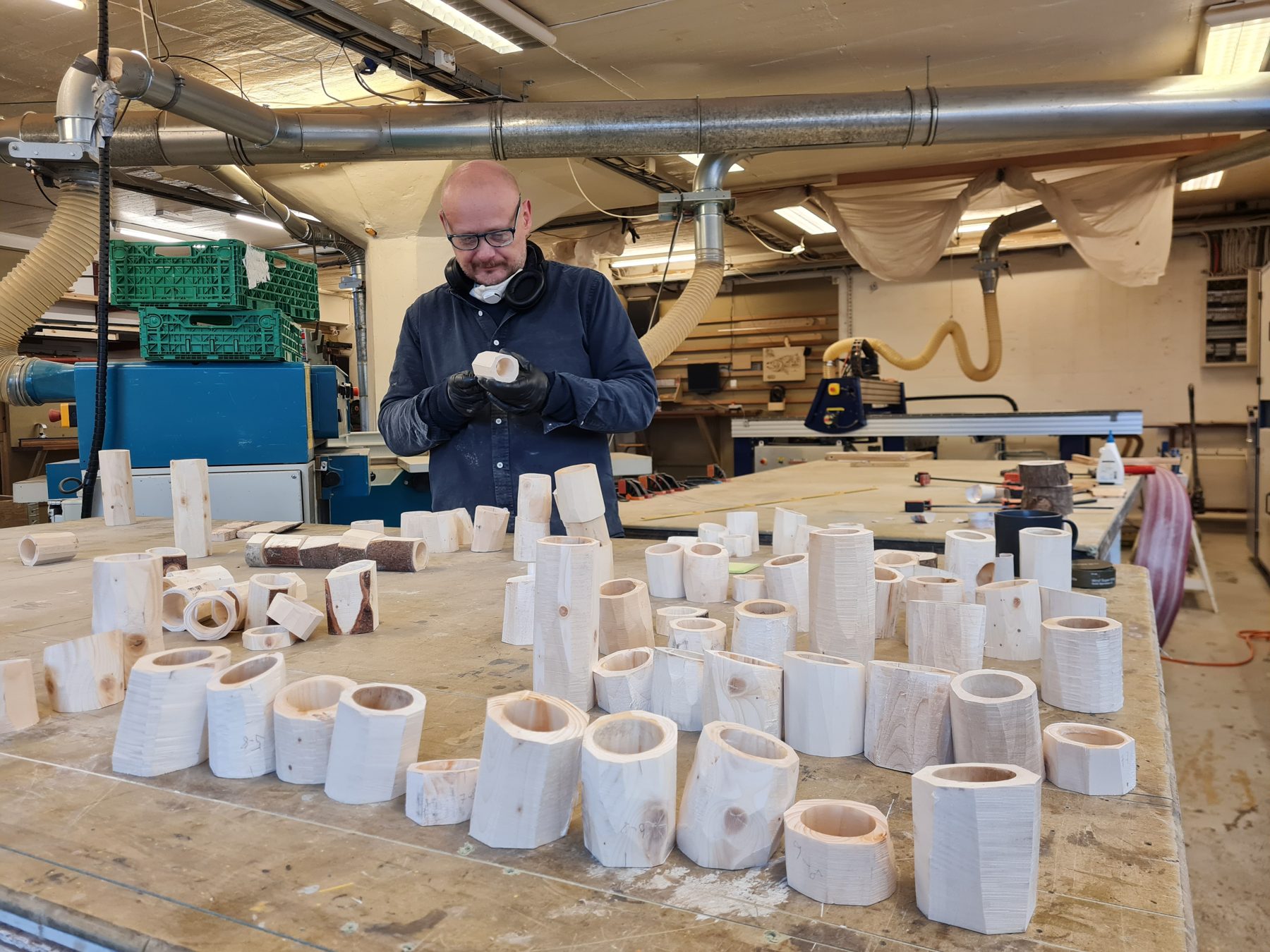 A workbench covered in dozens of turned and hollowed wooden pieces, with someone holding one up