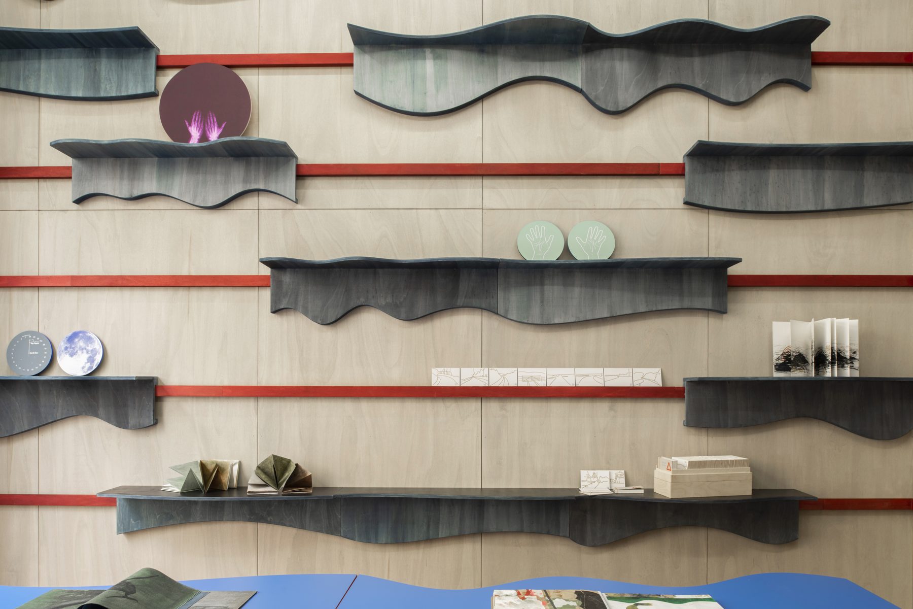 Wave-shaped blue-stained shelves on a plywood wall, with small objects displayed on them
